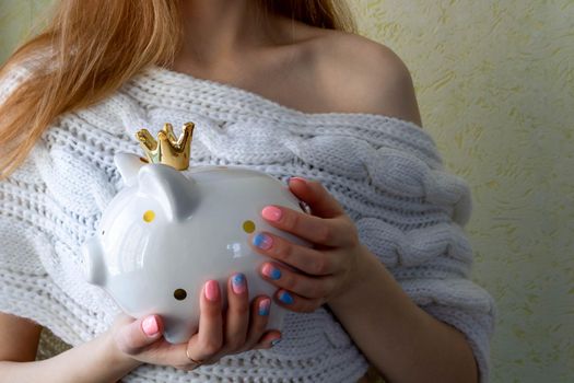 The girl's hands hold a white piggy bank with a golden crown.