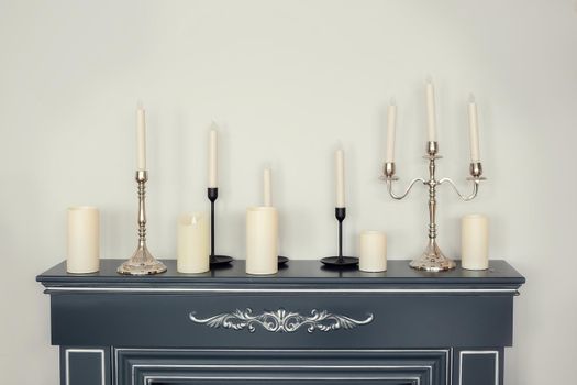 Candles of various types and sizes with and without candlesticks on the imitation fireplace countertop near the wall