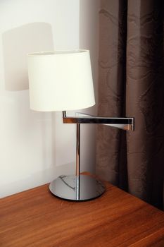 Stylish modern table lamp on a desk near a window with dark curtains.