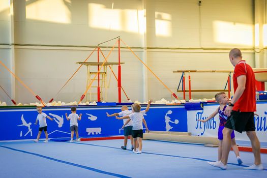 Small children, boys in training run in a circle in the hall under the guidance of a coach. Gymnastics. Moscow, Russia May 19, 2019