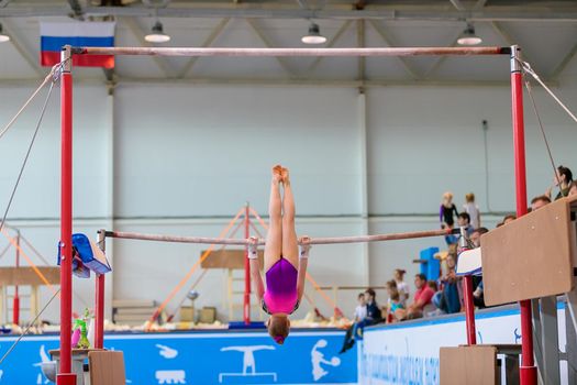A girl in sportswear performs an exercise on the uneven bars. Rhythmic gymnastics, training in the hall. Moscow, Russia May 19, 2019