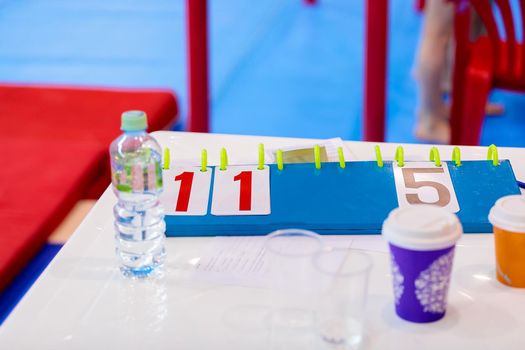 A plate with numbers for the jury's marks on the table with water and glasses. Artistic gymnastics competition