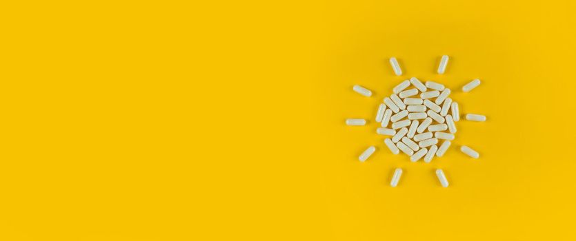 Sun shape made from white pills capsules on a yellow backdrop with copy space.