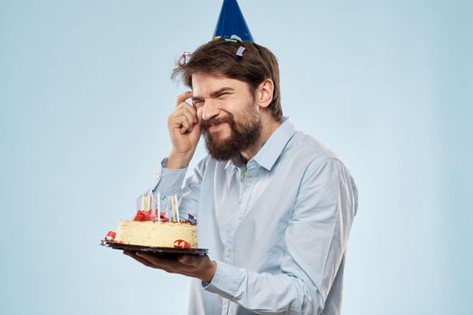 A man in a shirt with a cake in his hands and a festive cap on his head. High quality photo