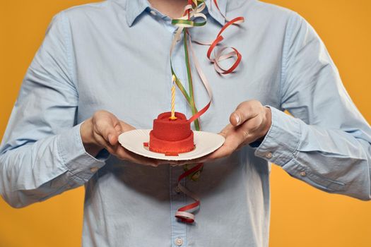 Cheerful man with a cake on a yellow background birthday holidays cap on his head. High quality photo