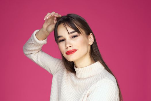 Brunette with long hair red lips cosmetics white sweater pink background cropped view. High quality photo