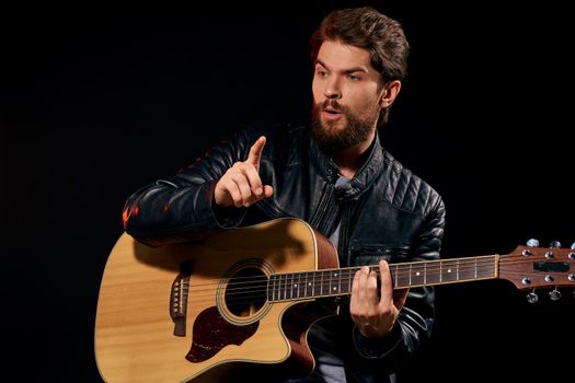 A man with a guitar in his hands leather jacket music performance rock star modern style dark background. High quality photo