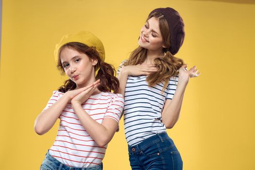 Cheerful sisters in hats striped T-shirts joy lifestyle yellow background family. High quality photo