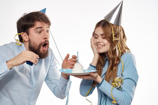 energetic man and woman with a cake and in hats celebrate a birthday on a light background. High quality photo