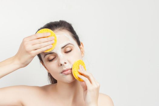 brunette with bare shoulders face mask sponges in hands. High quality photo