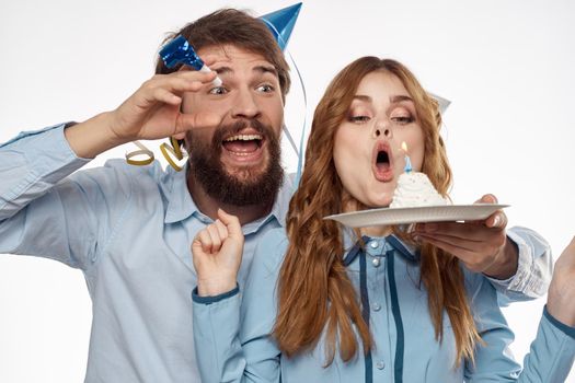 energetic man and woman with a cake and in hats celebrate a birthday on a light background. High quality photo