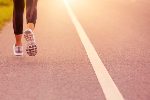 Close up Sporty woman running on road at sunset. Fitness and workout wellness concept.