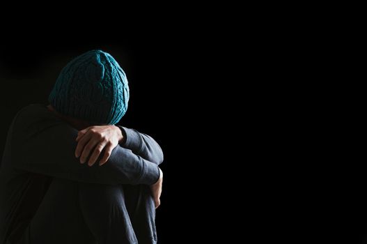 Sad woman hug her knee with depression sitting alone on the floor in the dark room, Black background