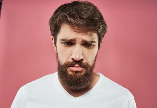 Sad man crying on a pink background in a white t-shirt cropped view. High quality photo