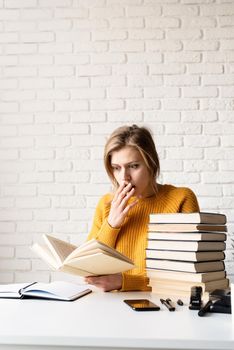 Young smiling woman in yellow sweater reading a book looking shocked or surprised
