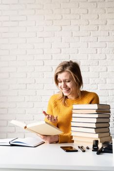 Young smiling woman in yellow sweater studying using laptop and reading a book