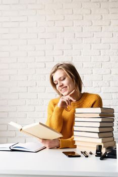 Young smiling woman in yellow sweater laughing reading a book