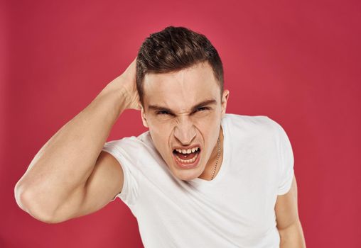 emotional man angry facial expression white t-shirt red background. High quality photo
