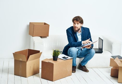 Business man sitting on the couch with laptop boxes with things unpacking . High quality photo