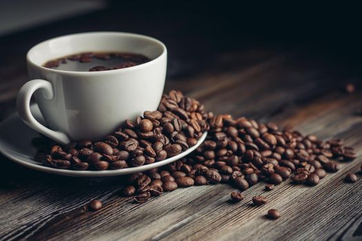 saucer with coffee beans and white cup on a wooden table side view Copy Space. High quality photo