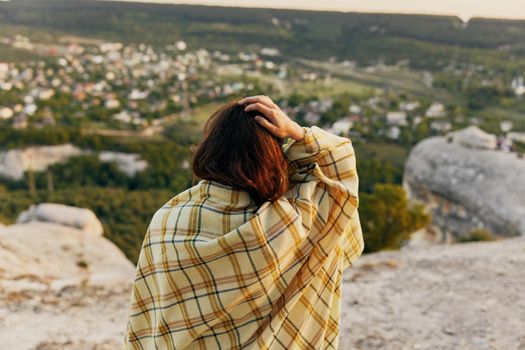 A woman with a blanket touches her head with her hand and looks at the village in the distance at nature. High quality photo