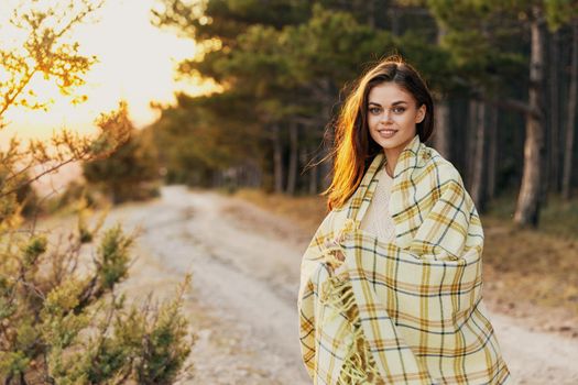 Happy woman tourist with a plaid on her shoulders near the coniferous forest. High quality photo