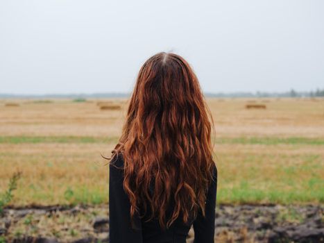 Beautiful woman with red hair in a black dress outdoors in the field. High quality photo