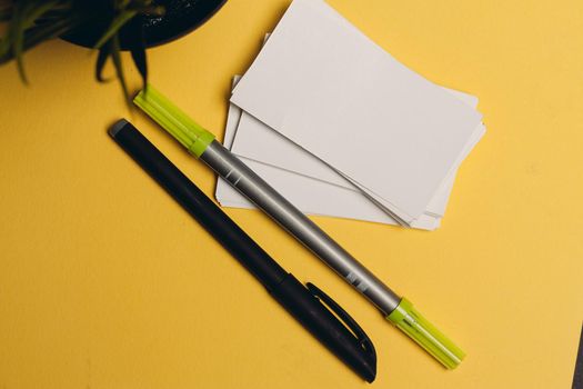 markers pens and rubber bands on a yellow background flowers in a pot and a cup of coffee. High quality photo