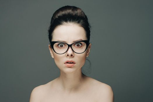 surprised woman with glasses naked shoulders gathered hair gray background. High quality photo