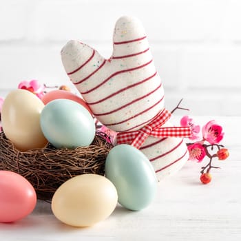 Close up of colorful Easter eggs in the nest with pink plum flower on bright white wooden table background.