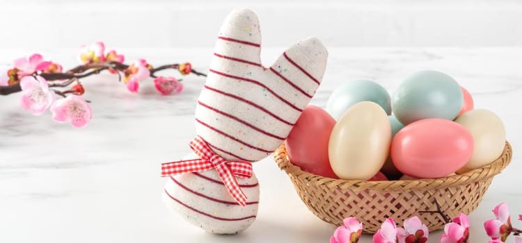 Close up of colorful Easter eggs in the nest with pink plum flower on bright white wooden table background.