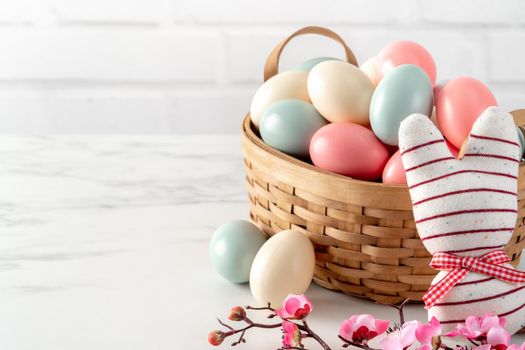 Close up of colorful Easter eggs in the nest with pink plum flower on bright white wooden table background.