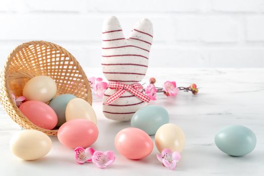 Close up of colorful Easter eggs in the nest with pink plum flower on bright white wooden table background.