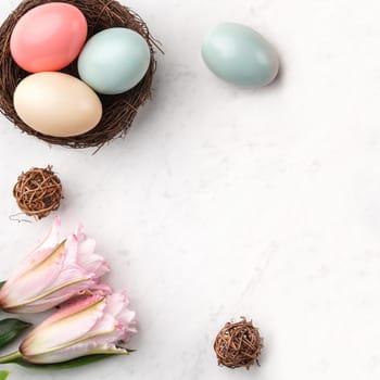 Colorful Easter eggs in the nest with pink lily flower on bright marble white table background.