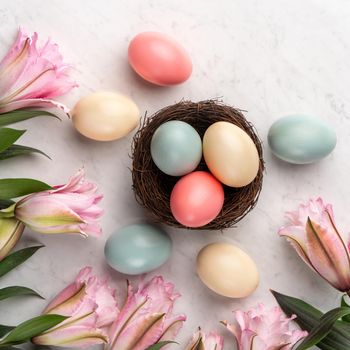 Colorful Easter eggs in the nest with pink lily flower on bright marble white table background.