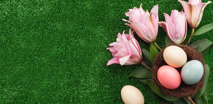 Colorful Easter eggs in the nest with pink lily flower on a lawn grass background.