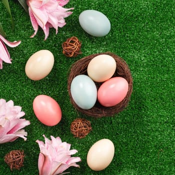 Colorful Easter eggs in the nest with pink lily flower on a lawn grass background.