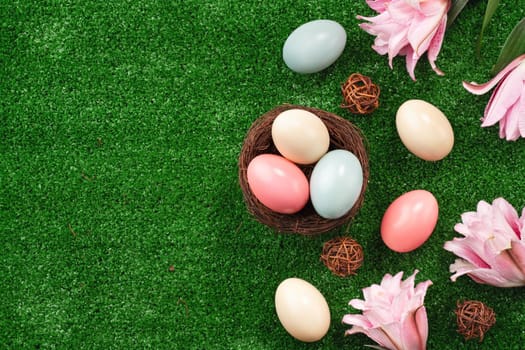 Colorful Easter eggs in the nest with pink lily flower on a lawn grass background.