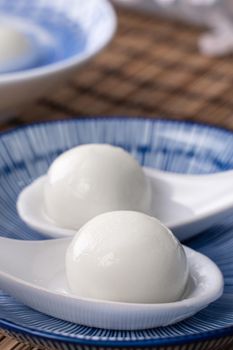 Close up of yuanxiao tangyuan (glutinous rice dumpling balls) in a bowl on gray table with flower, food for Chinese Lantern Yuanxiao Festival.
