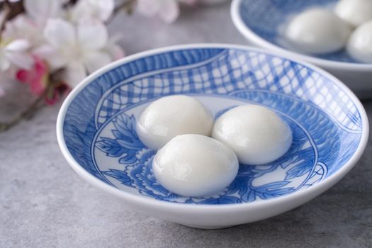 Close up of yuanxiao tangyuan (glutinous rice dumpling balls) in a bowl on gray table with flower, food for Chinese Lantern Yuanxiao Festival.