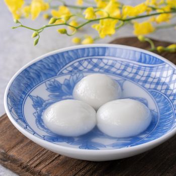 Close up of yuanxiao tangyuan (glutinous rice dumpling balls) in a bowl on gray table with flower, food for Chinese Lantern Yuanxiao Festival.