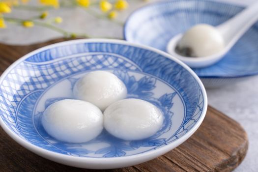 Close up of yuanxiao tangyuan (glutinous rice dumpling balls) in a bowl on gray table with flower, food for Chinese Lantern Yuanxiao Festival.