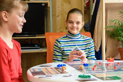 Children in a good mood are playing a board game, one of the girls looked into the frame