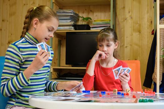A girl plays a card from her hand, another girl looks thoughtfully