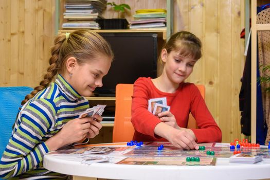 Children play a board game, one of the girls makes the next move, the other watches with a smile
