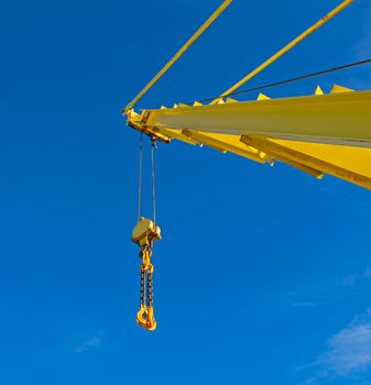 Large extended industrial crane jib boom arm against a blue sky background with block tackle