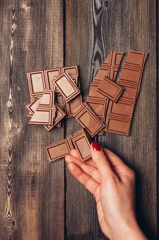 female hand and broken bar of chocolate on wooden table portrait. High quality photo