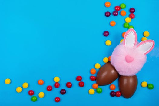 Easter concept, candy jelly beans, chocolate egg, pink rabbit head toy on a blue background. Place for text