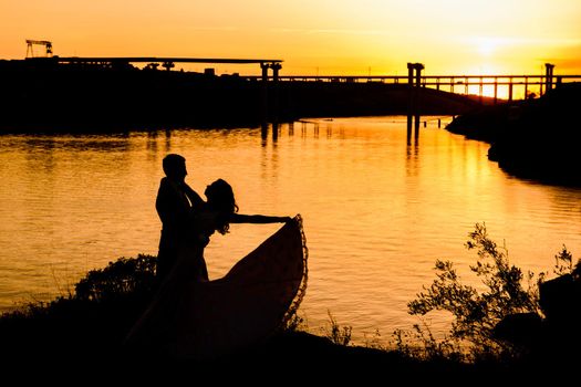 silhouettes of a happy young couple guy and girl on a background of orange sunset in the sand desert