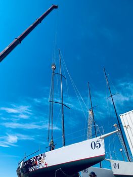 Russia, St.Petersburg, 26 May 2020: Port Hercules, the big industrial crane lifts the sailboat and floats it, the beginning of a season of sailing, a skyscraper on a background, sailboat is groundless, sunny weather